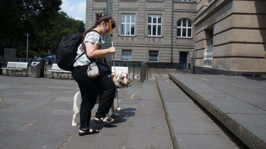 Die blinde Studentin Carina und ihr Blindenführhund Pitou gehen eine Treppe der TH Köln hinauf