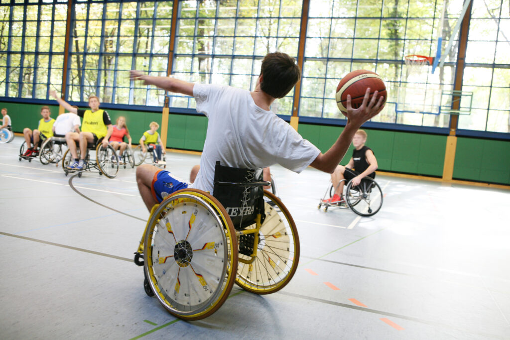 Mehrere Menschen spielen Rollstuhlbasketball in der Turnhalle der Deutschen Sporthochschule Köln